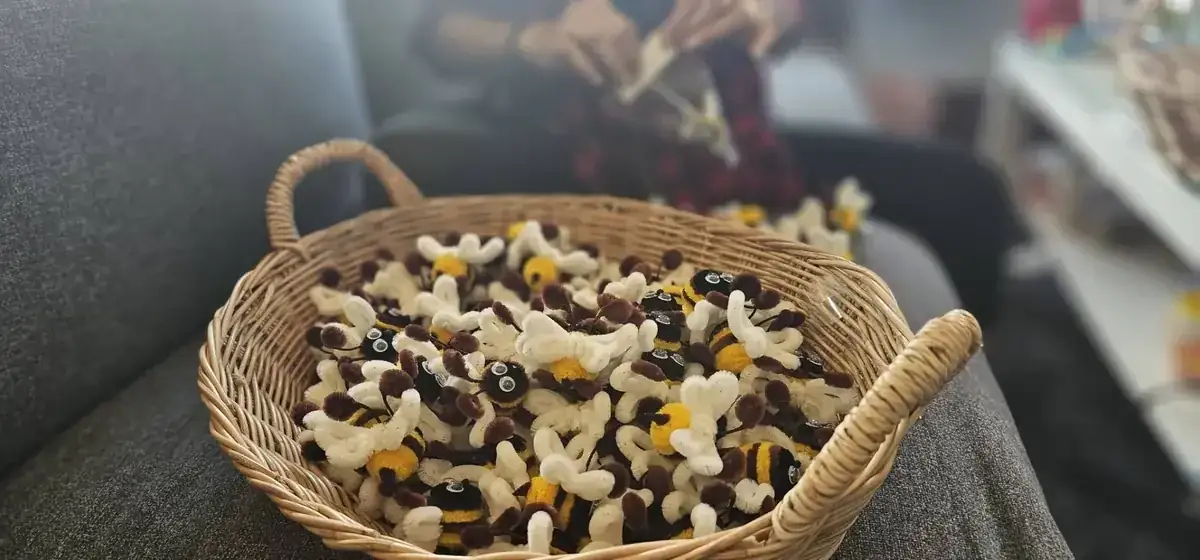 Wicker basket full of handmade pipe cleaner bees with worker in background
