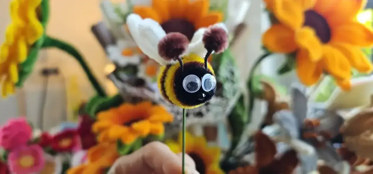 Handmade pipe cleaner bee with googly eyes among colorful sunflowers - Save the Bees Thailand